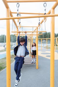 A boy in a school uniform enjoys playing on monkey bars outdoors.